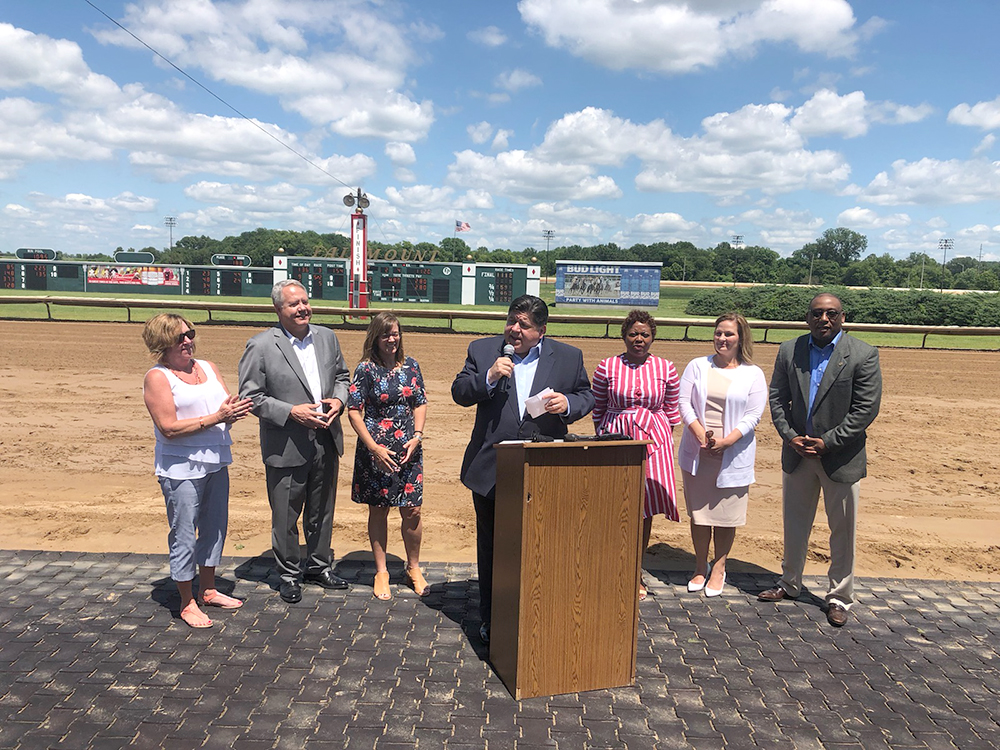 Rep. Bristow, Rep. Hoffman, Rep. Stuart, Gov. JB Pritzker, Rep. Greenwood, Sen. Crowe and Sen. Belt address the crowd at Fairmount Park Race Track in Collinsville